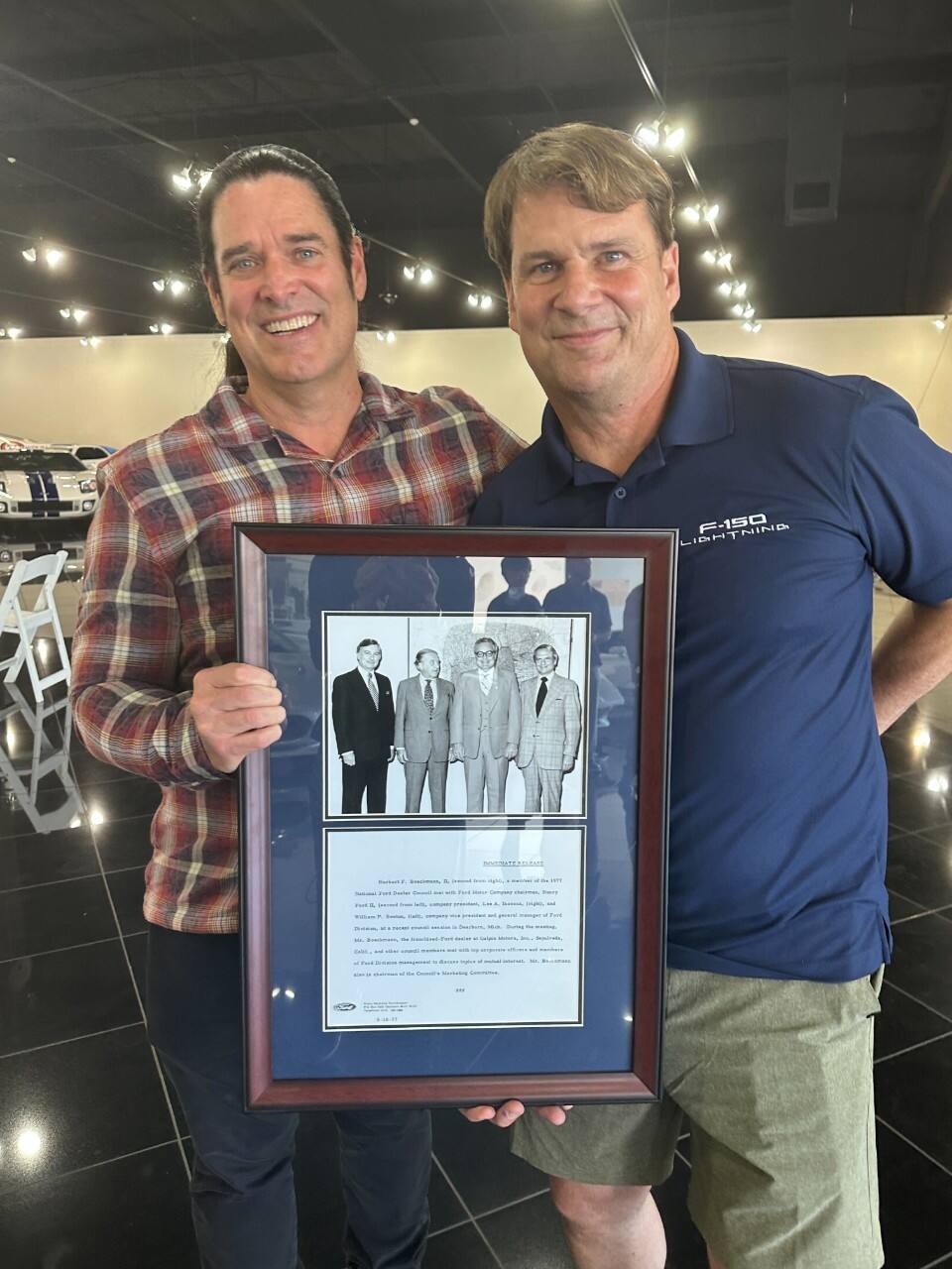 m Farley and Beau Boeckmann pose for a photo, holding a framed image and news clipping honoring Beau’s father, Bert.
